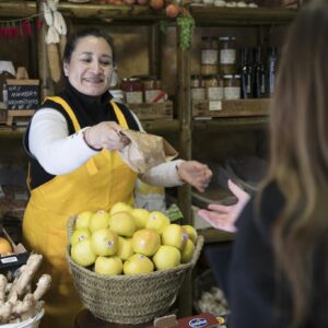 Smiling woman vendor handing a bag to a customer in a Madrid grocery store.