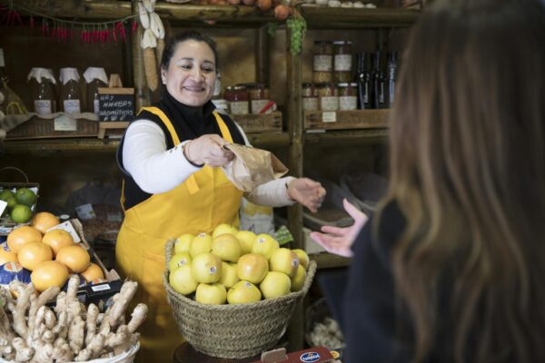 Smiling woman vendor handing a bag to a customer in a Madrid grocery store.