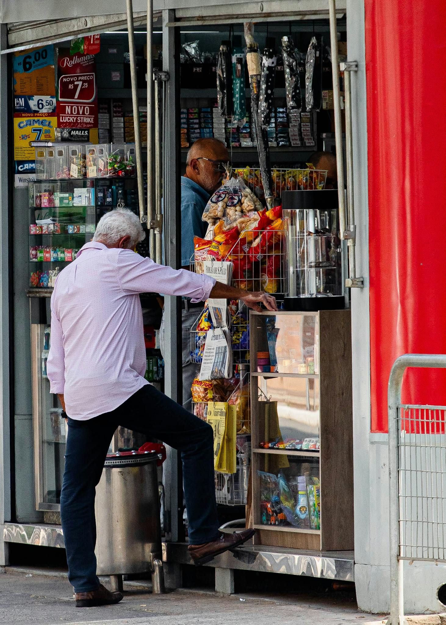Two men at a street vendor stall exchanging goods in a bustling urban area.
