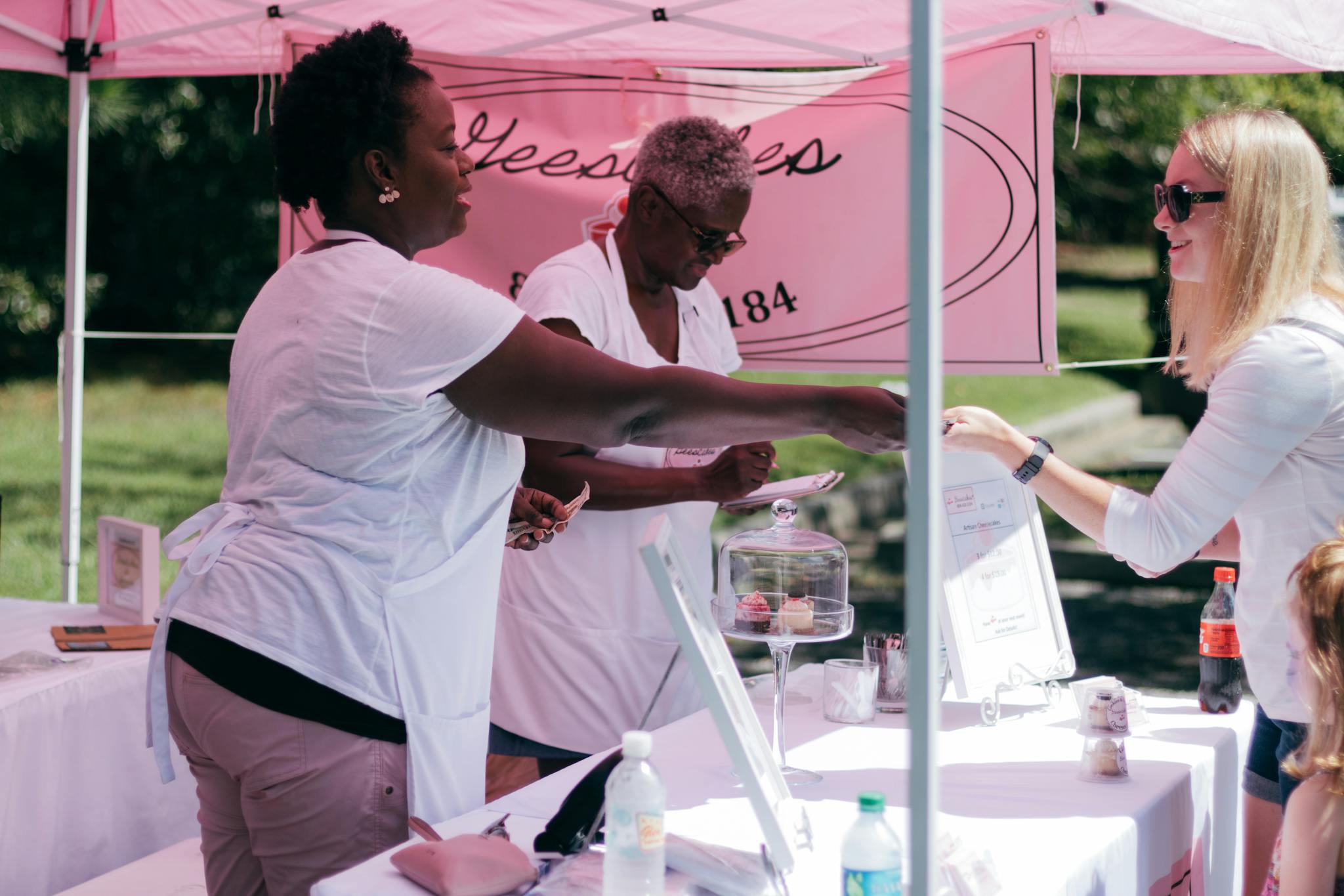 Two women selling goods to a customer at an outdoor stall during the day.